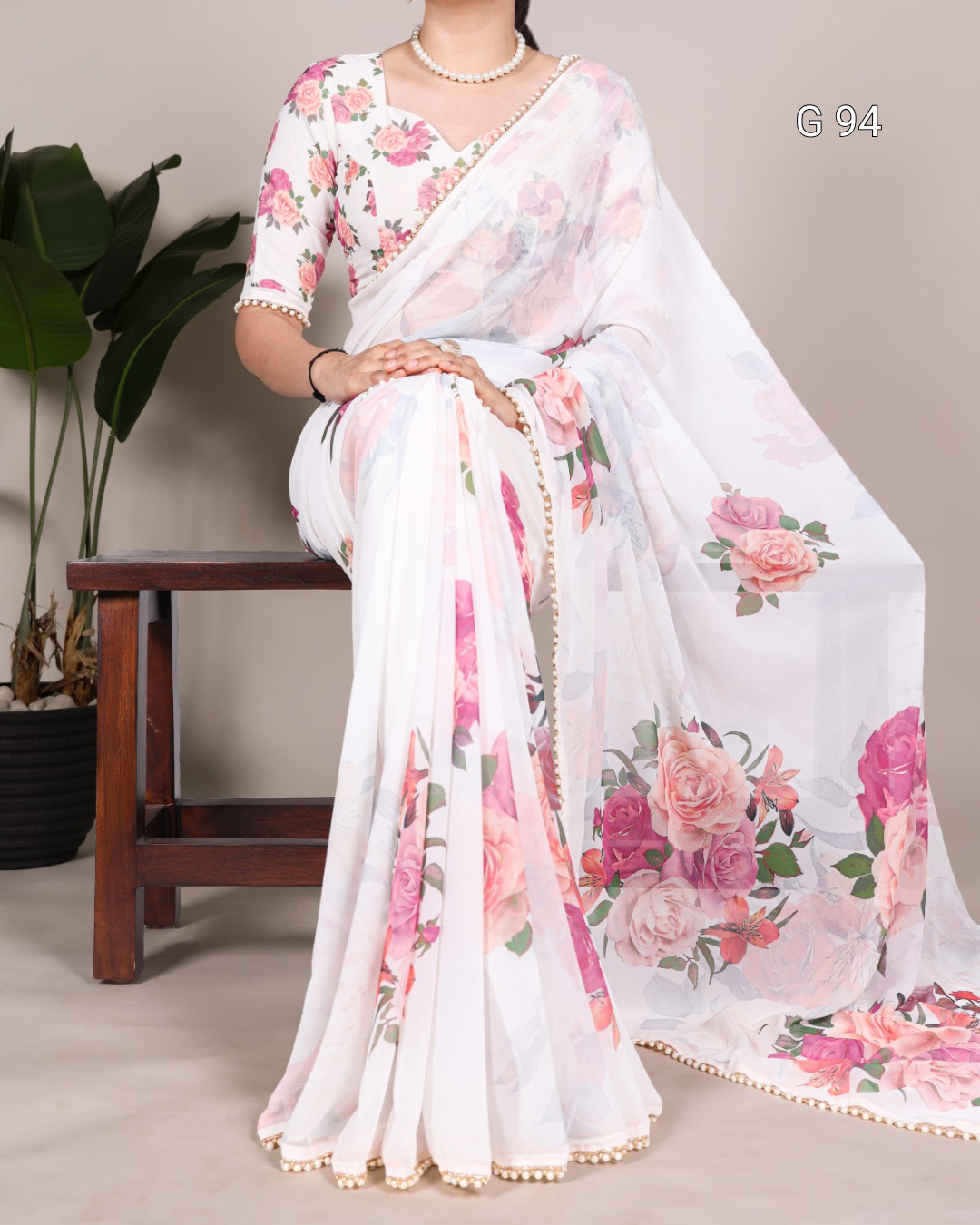 Woman wearing a floral saree sitting on a chair with a plant in the background