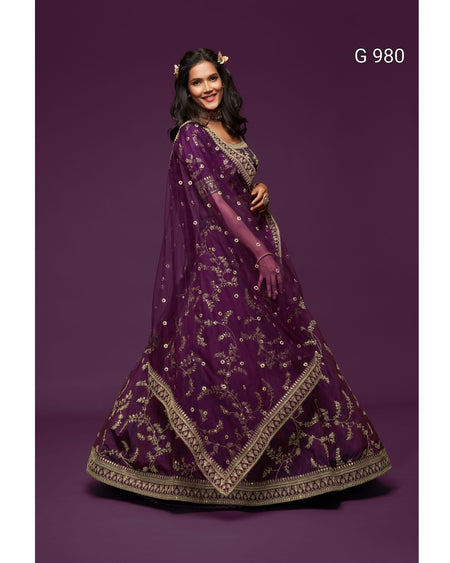 A woman modeling a deep purple traditional Indian lehenga choli set with intricate gold embroidery, set against a solid dark purple studio background. The text 'G 980' is visible in the top right corner.