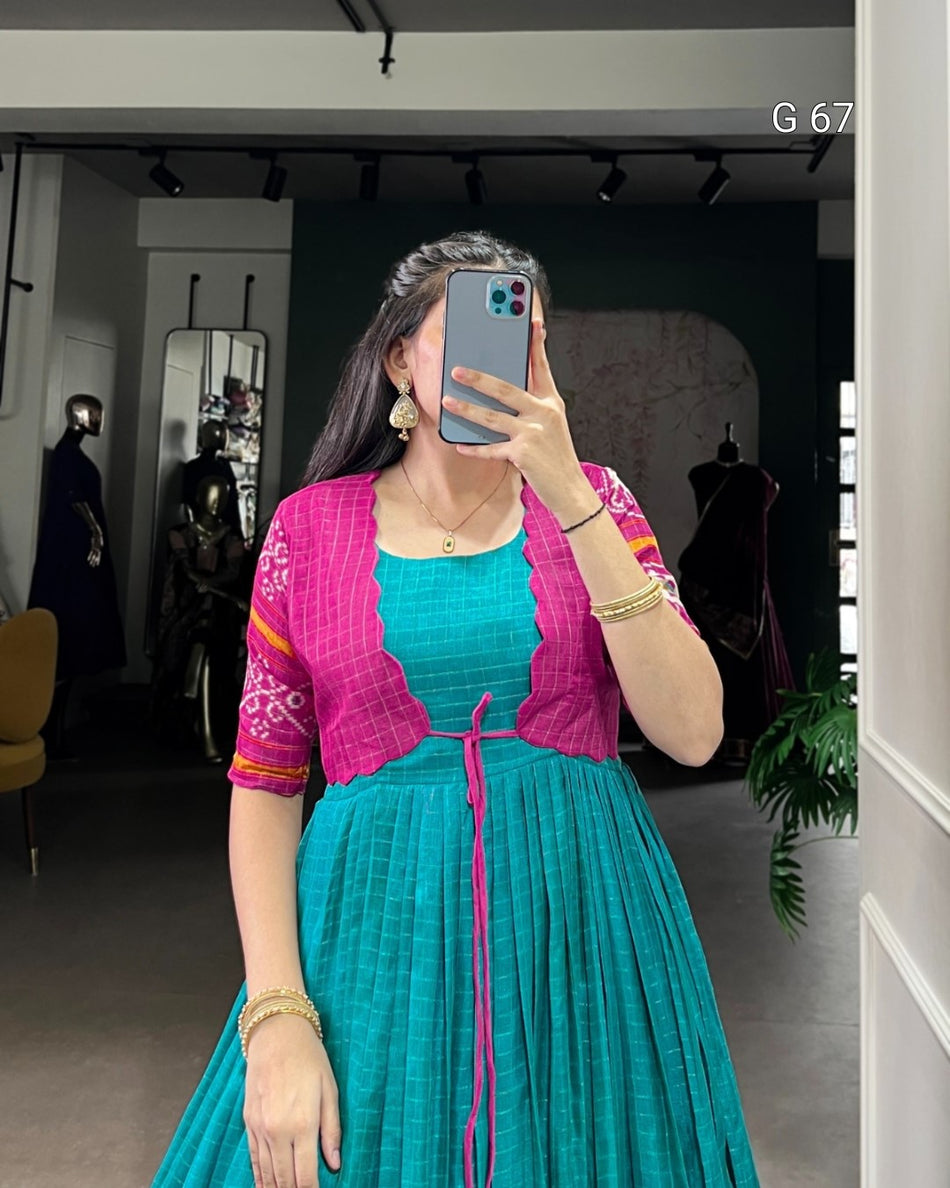 Woman taking a mirror selfie wearing a teal dress with a pink jacket in a room.