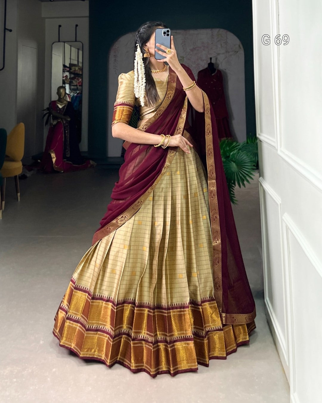 Woman wearing a traditional maroon and gold saree taking a mirror selfie.