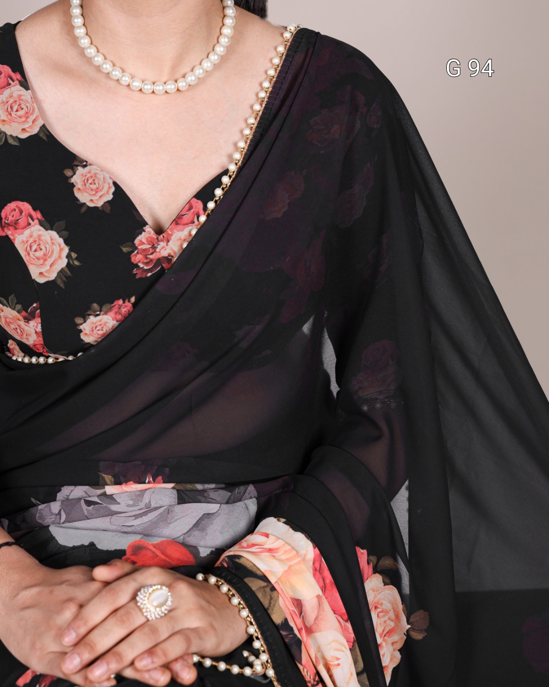 Black saree with floral patterns and pearl jewelry on a neutral background
