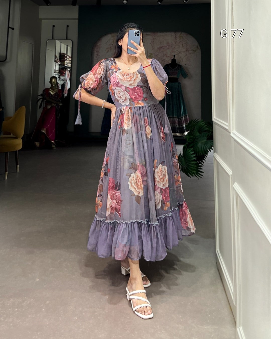 Woman wearing a floral dress taking a mirror selfie in an indoor setting.