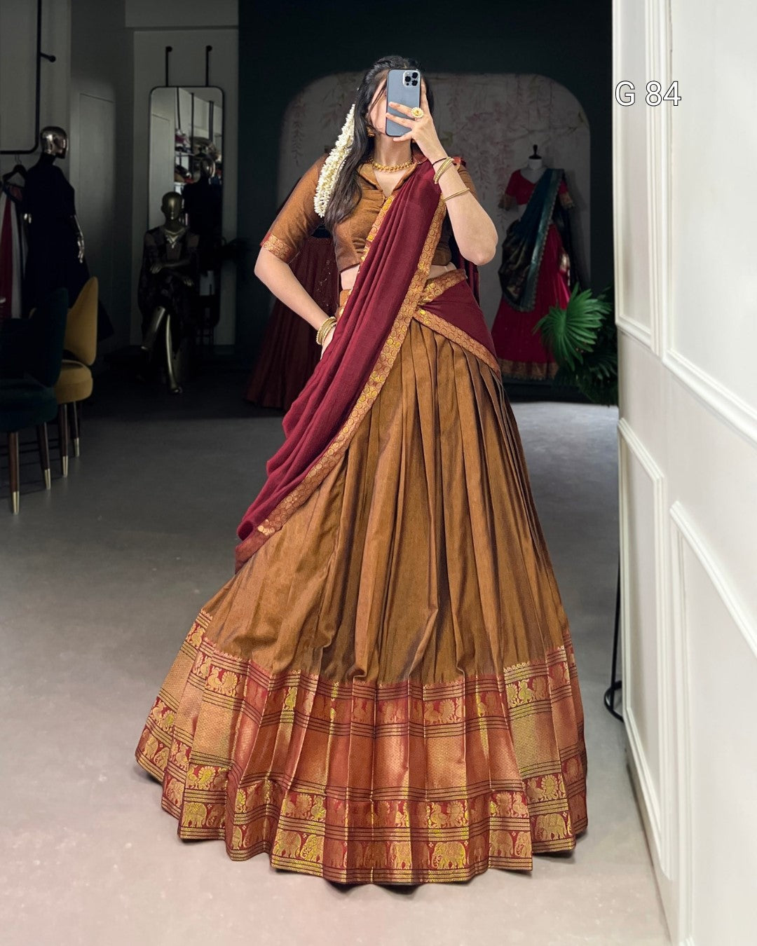 Woman wearing a traditional brown and red saree in a room with mirrors and clothing.