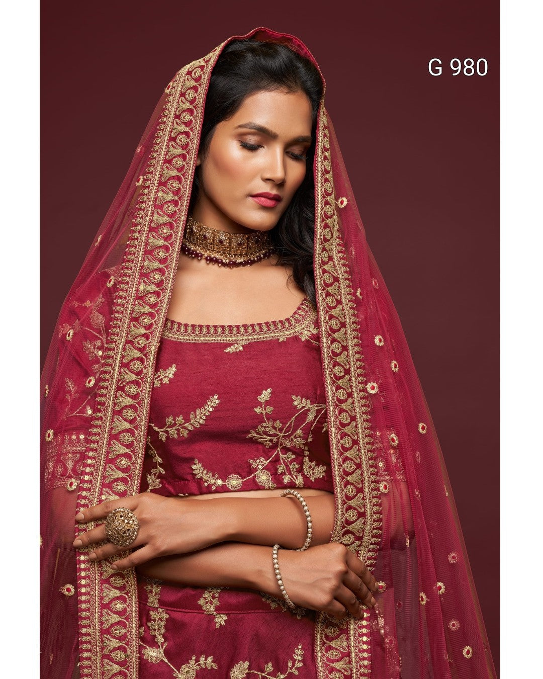 A woman wearing a deep maroon traditional outfit with gold embroidery and a matching sheer dupatta, posed against a solid maroon background. The text 'G 980' is visible in the top right corner.