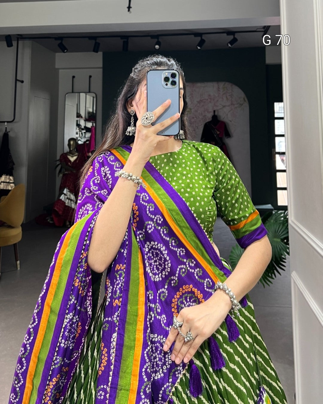 Person wearing a colorful saree with a patterned border, taking a mirror selfie.