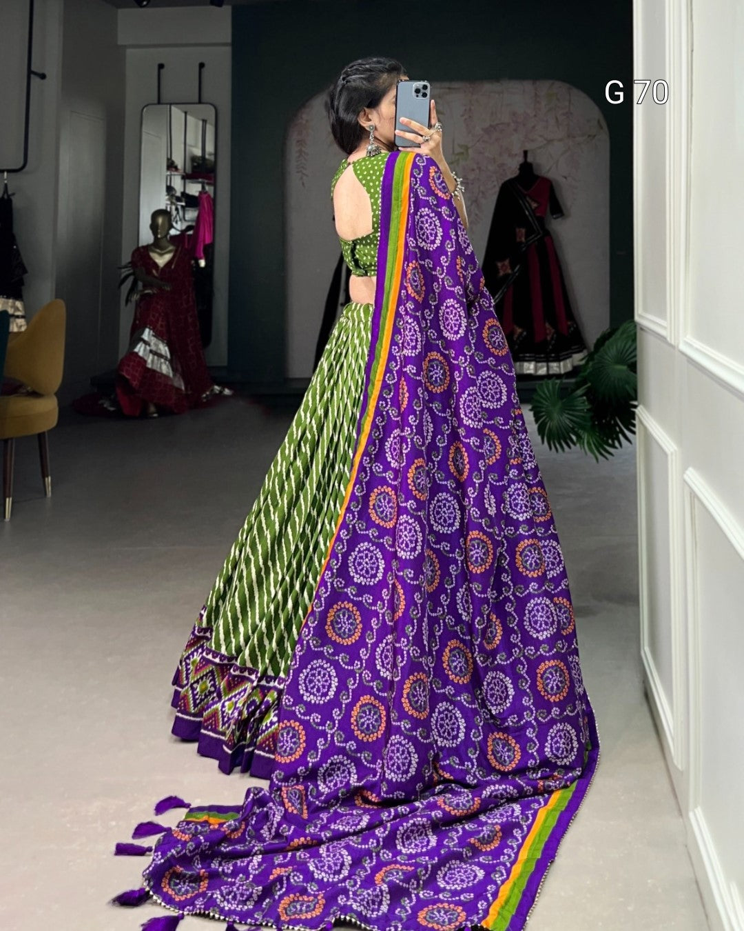 Person wearing a green and purple traditional outfit with a colorful border, standing in a room.