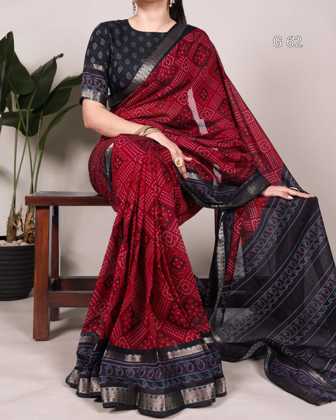 Woman wearing a red and black patterned saree with a plant in the background