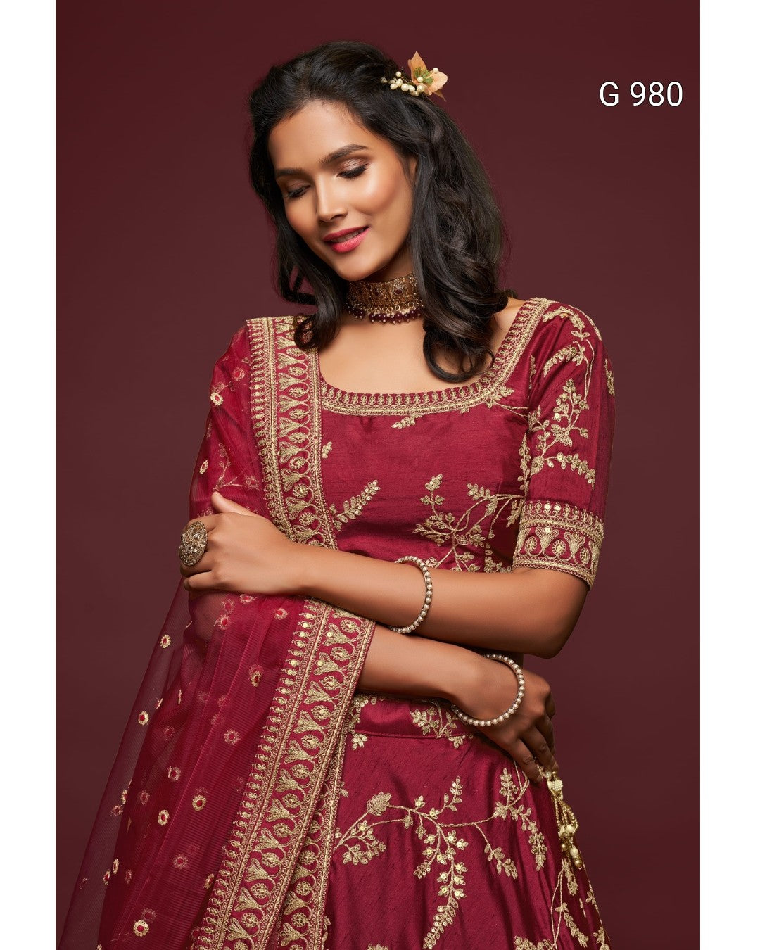 A woman modeling a deep maroon traditional outfit with gold floral embroidery and a matching dupatta, set against a solid maroon background. The text 'G 980' is visible in the top right corner.