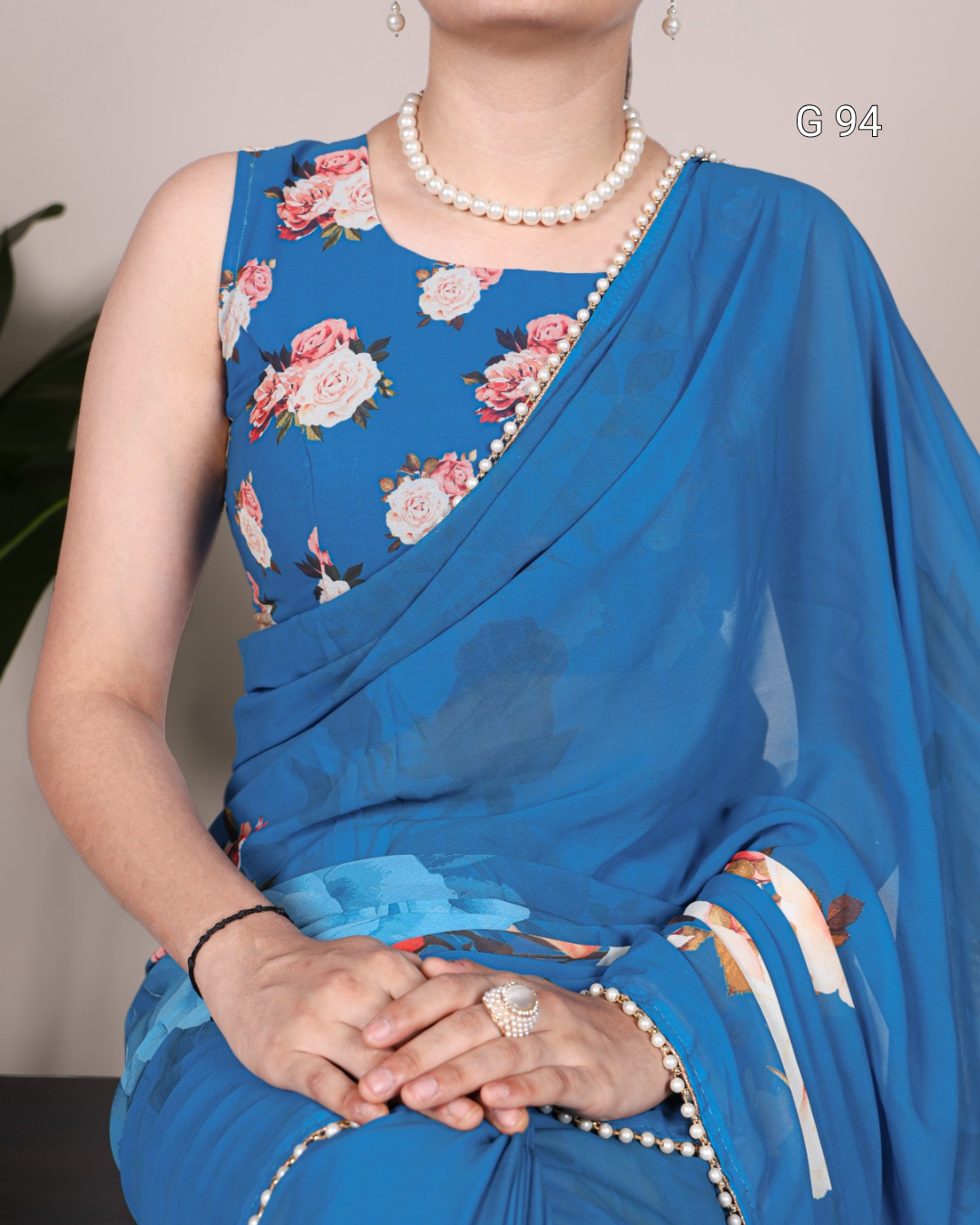 Woman wearing a blue saree with floral patterns and a pearl necklace.