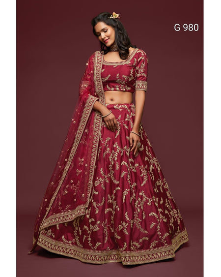 A woman modeling a deep maroon lehenga choli set with intricate gold floral embroidery, set against a solid maroon background. The text 'G 980' is visible in the top right corner.