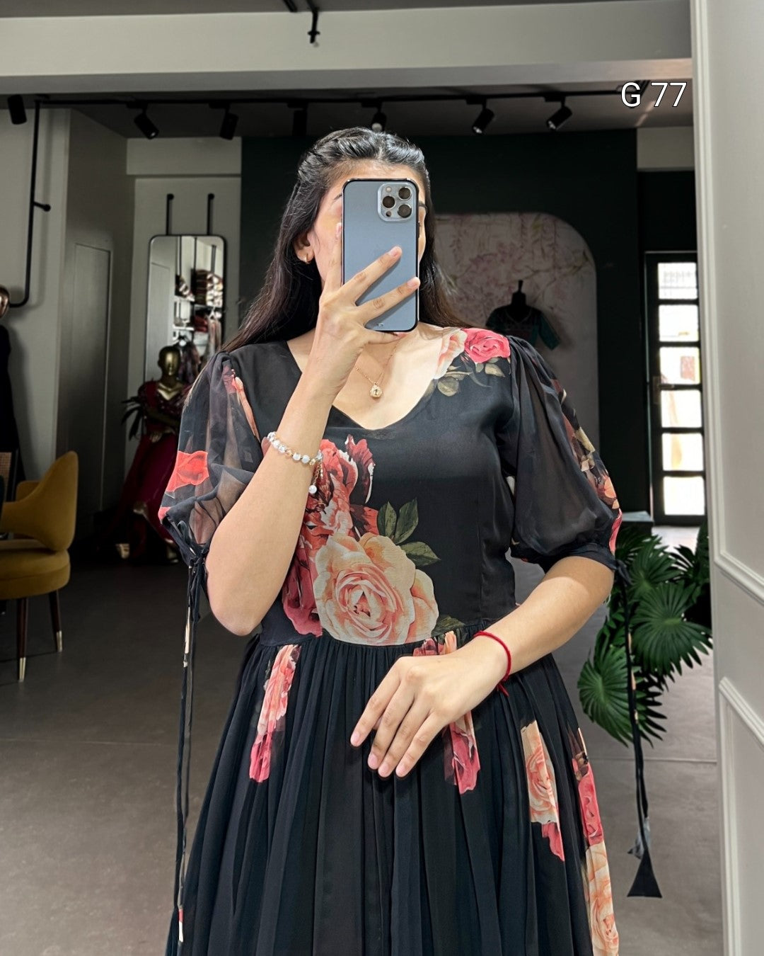 Woman taking a mirror selfie wearing a black dress with floral designs in a room.