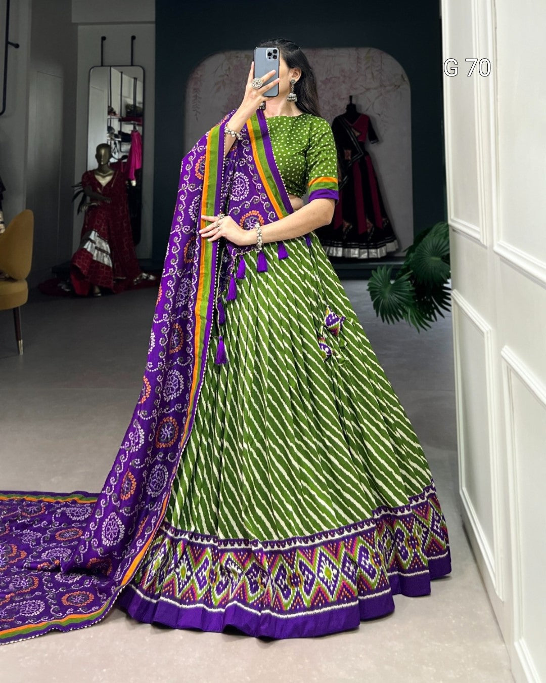 Woman taking a mirror selfie wearing a green and purple traditional outfit with a matching dupatta.