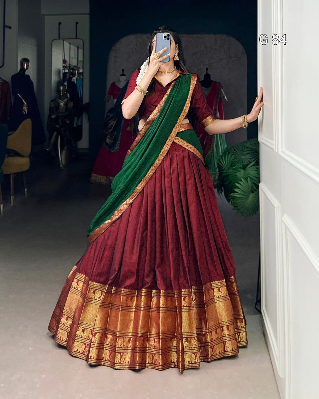 Person wearing a traditional maroon and green saree with gold border in a room.
