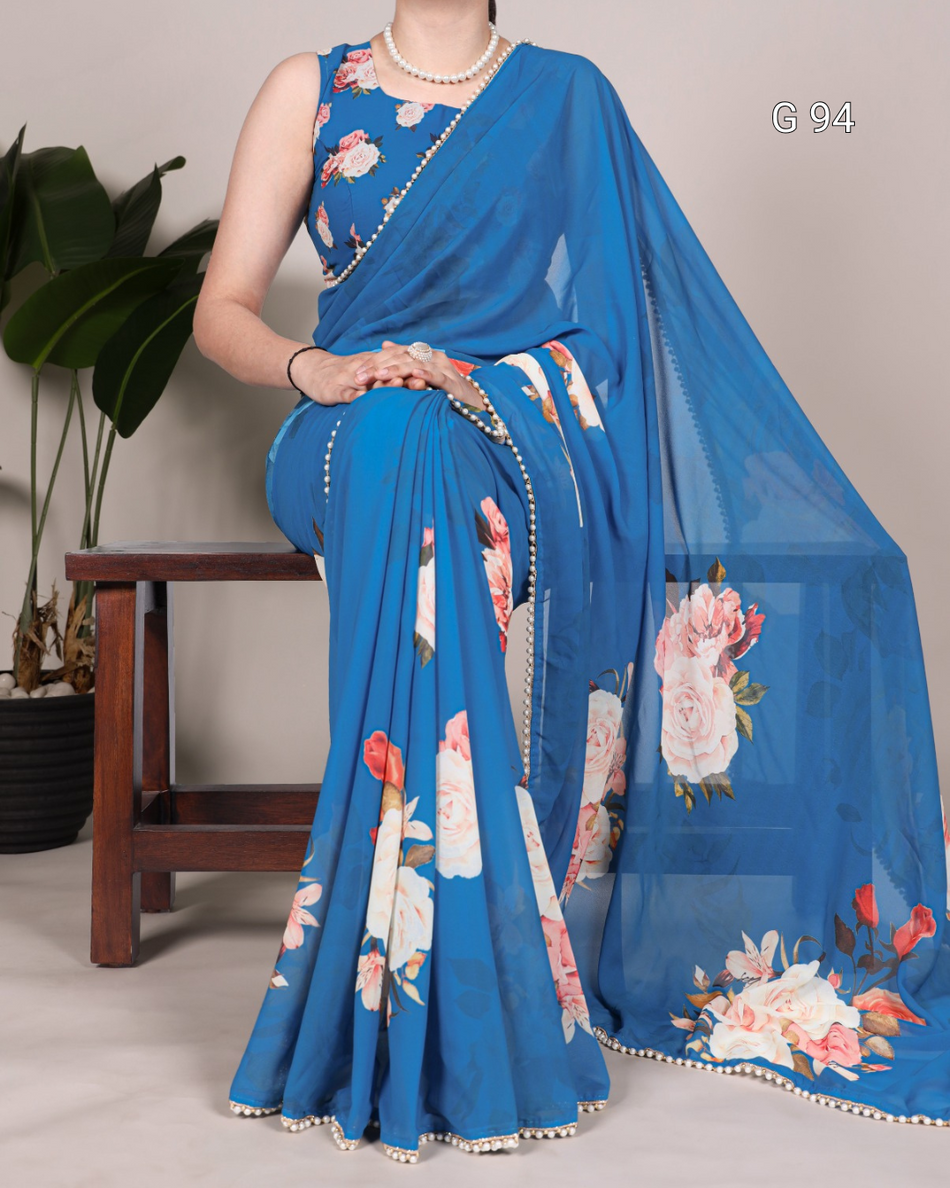 Woman wearing a blue saree with floral patterns, sitting on a chair.