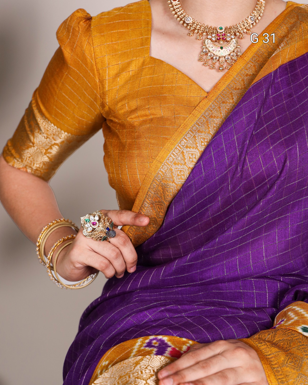 Person wearing a mustard yellow blouse with a purple saree, holding a ring.