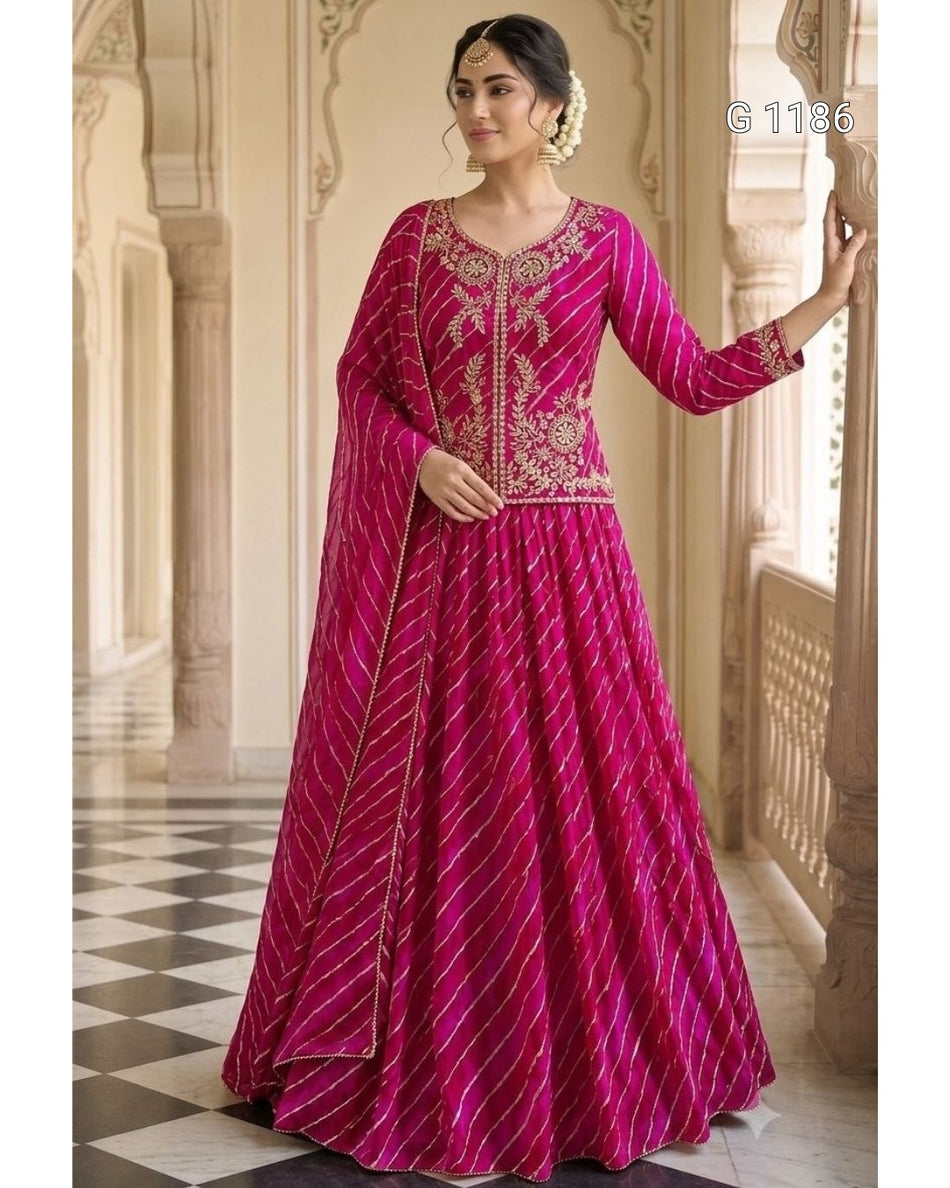 A woman models a bright magenta pink traditional Indian anarkali gown with gold zari embroidery and striped patterns, set against a classical architectural background with pillars.