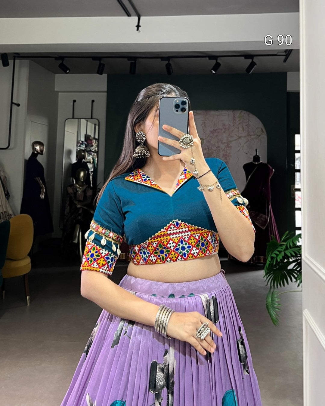 Person wearing a colorful traditional outfit with a blue top and purple skirt in a room.