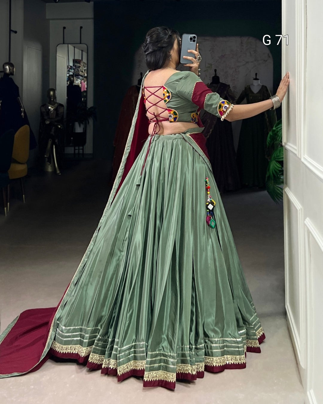Person wearing a green traditional outfit with red accents, standing in a room.