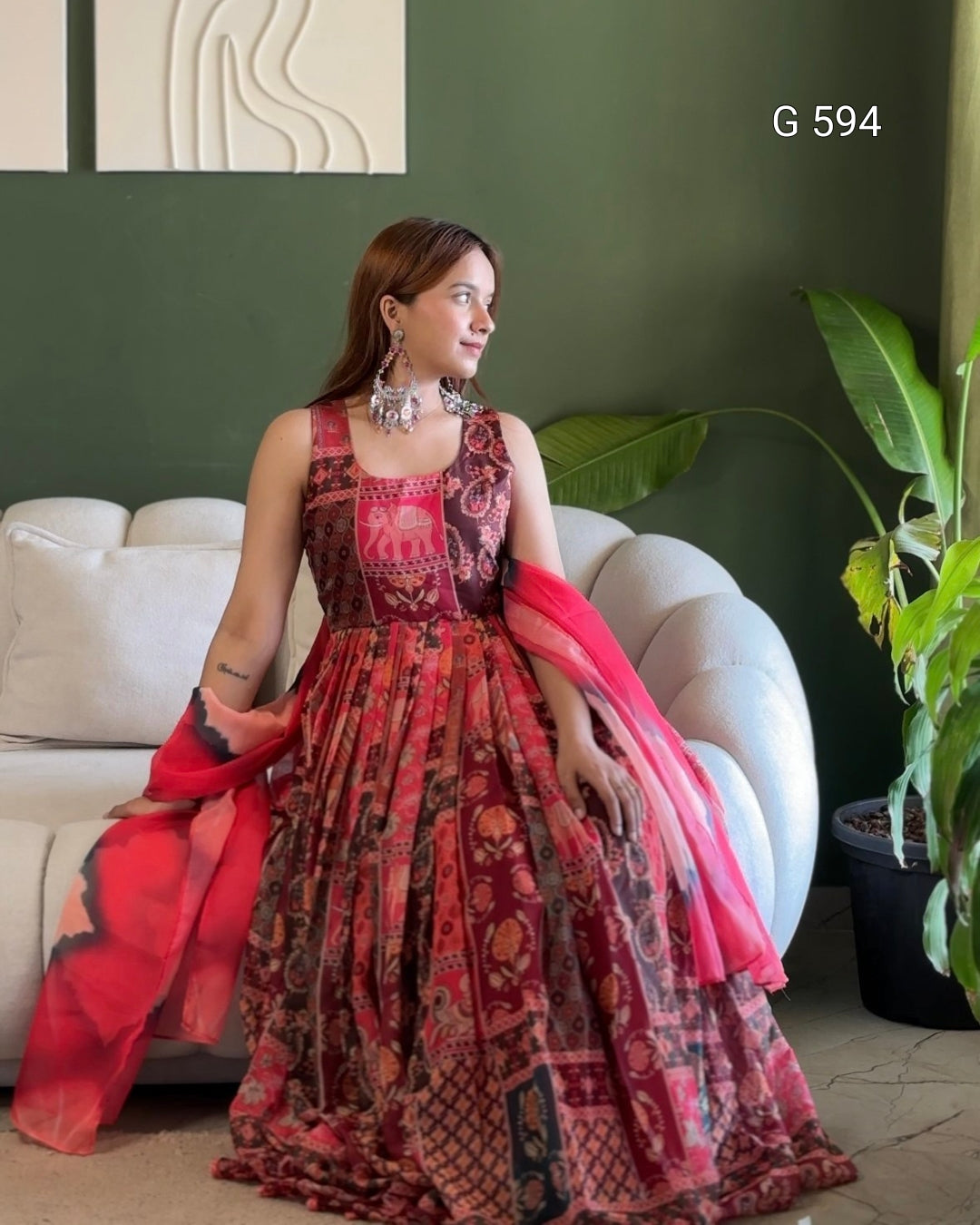 Woman in a red and black patterned dress with a pink dupatta sitting on a white couch.