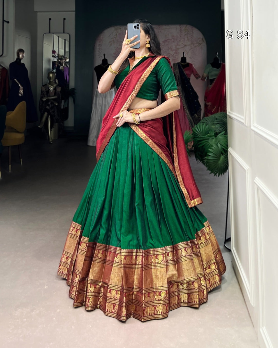 Woman wearing a green and red saree with gold border in a room.