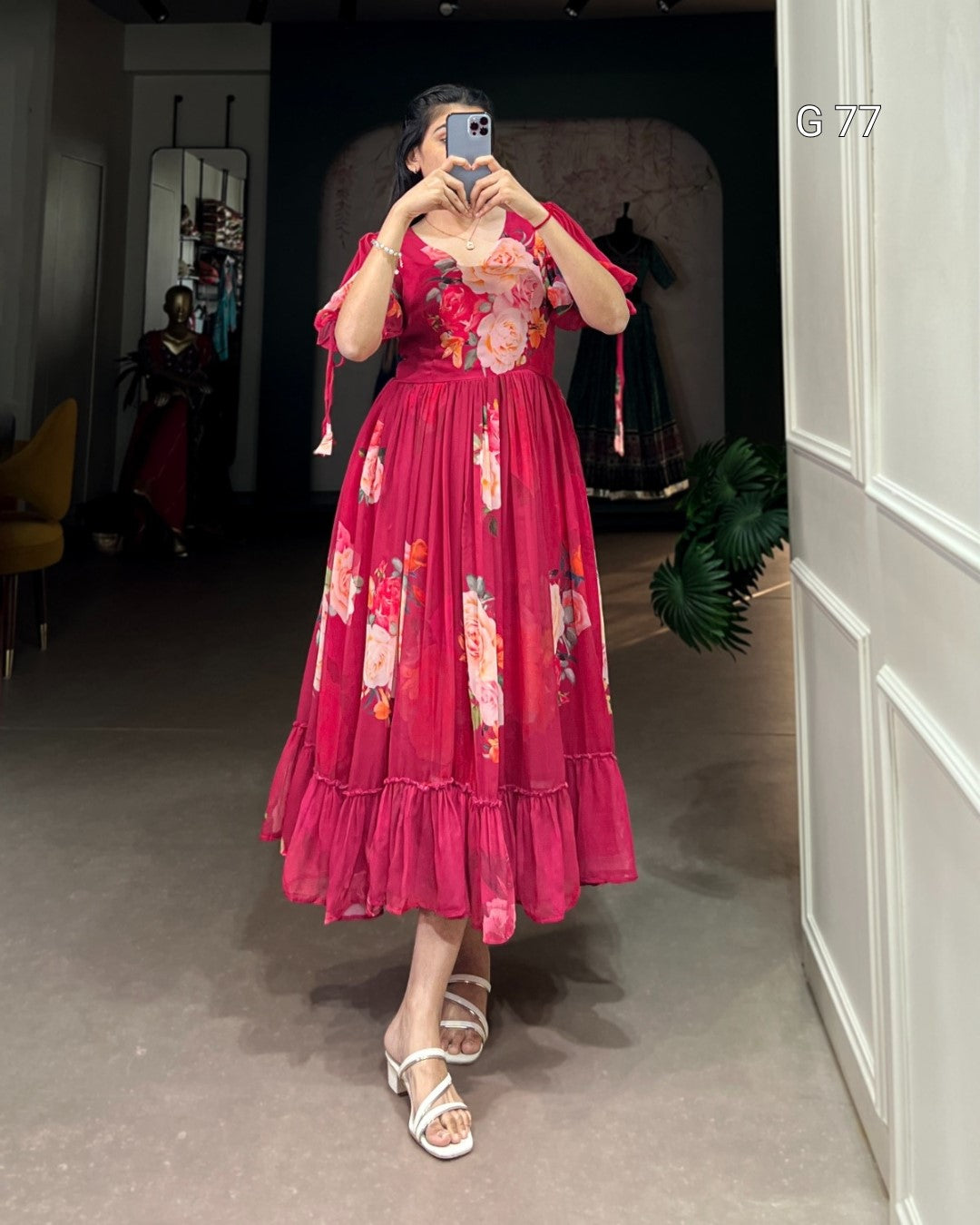 Woman wearing a red floral dress taking a mirror selfie in an indoor setting.