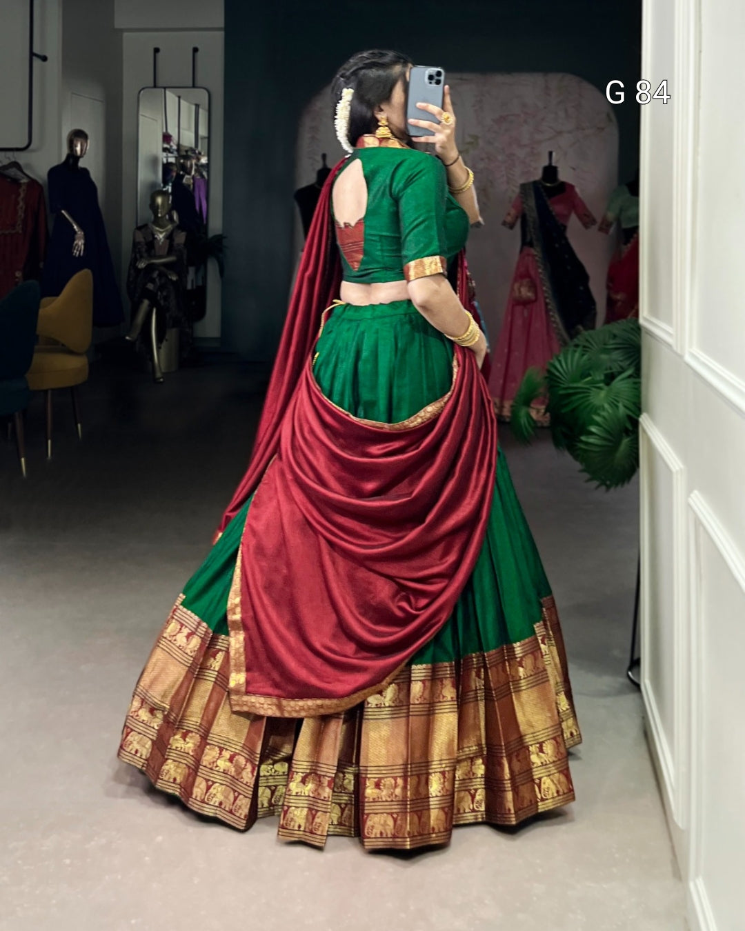 Person wearing a green and red traditional outfit with gold details, standing in a room.