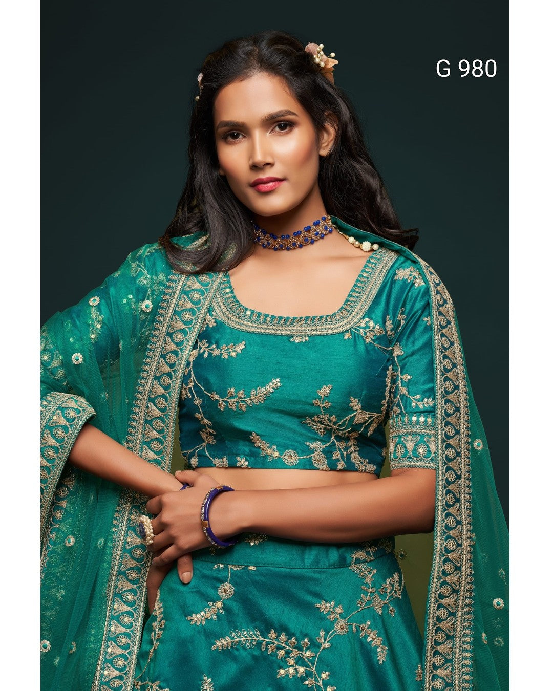 A woman modeling a teal green embroidered traditional outfit with a matching sheer dupatta, featuring gold floral embroidery and mirror work, set against a dark background with the text 'G 980' in the top right.