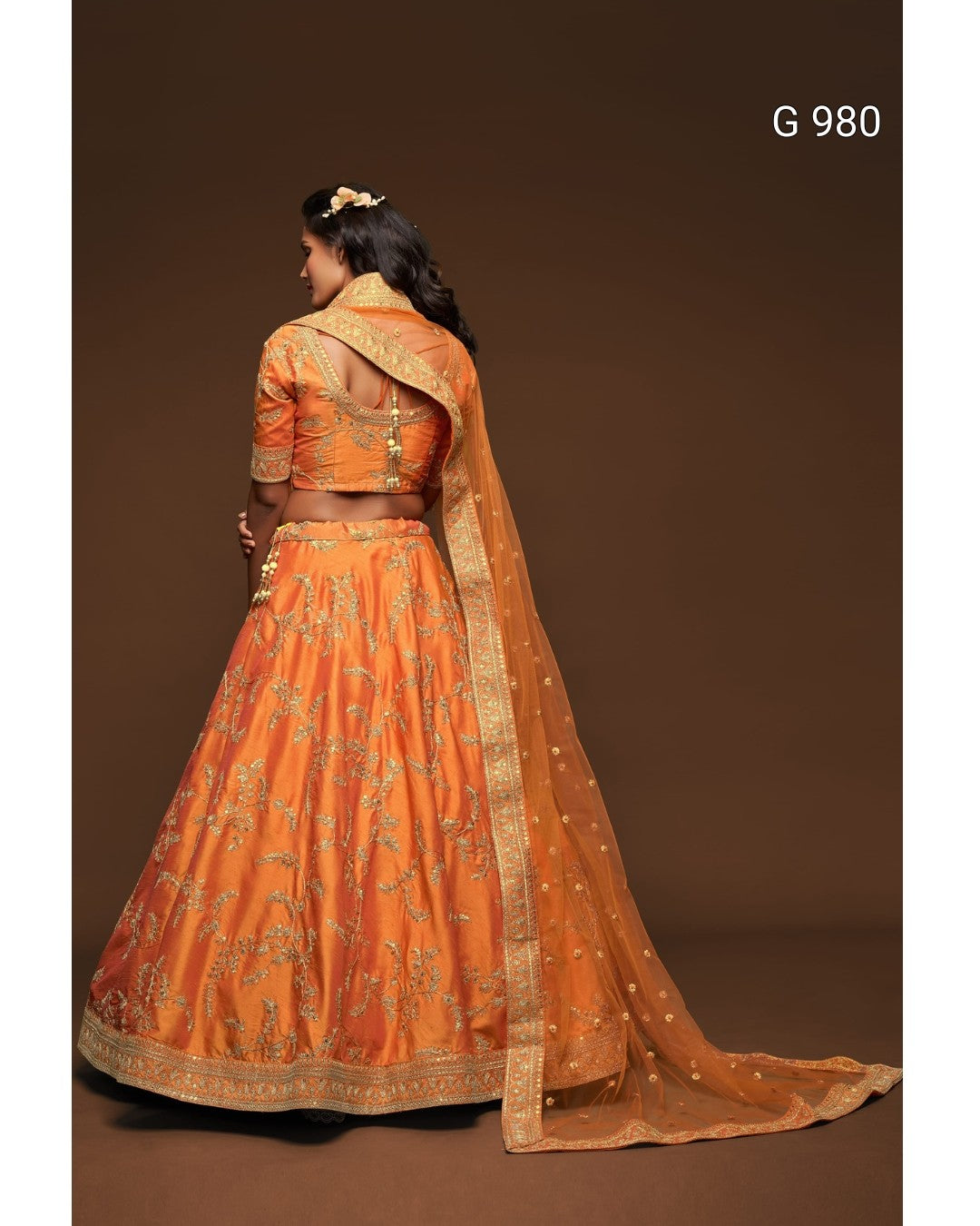 An orange embroidered lehenga choli set with a matching dupatta, shown on a model from the back against a dark brown studio background. The text 'G 980' is visible in the top right corner.