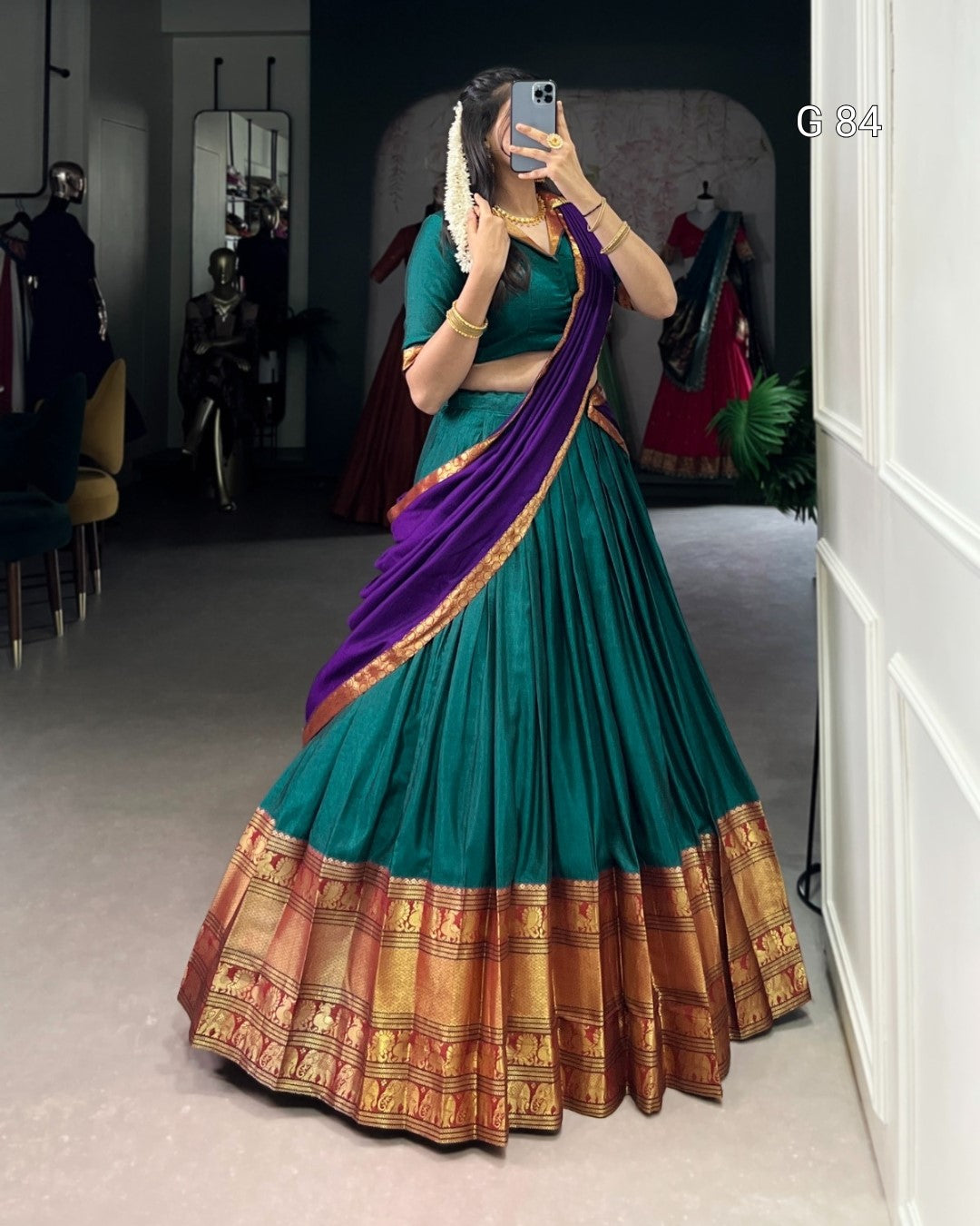 Woman wearing a traditional teal and purple saree with a gold border, standing in a room.