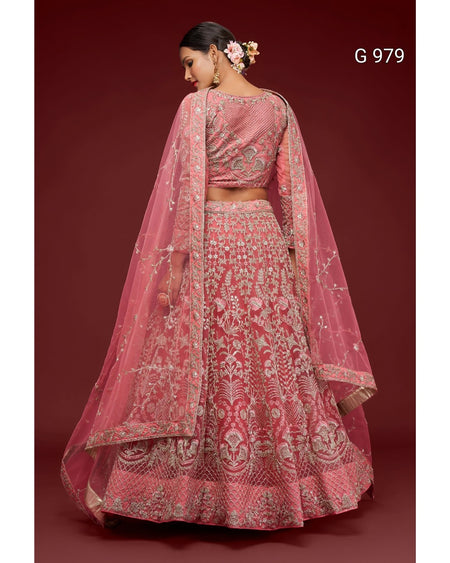 A pink heavily-embroidered Indian ethnic lehenga choli set with a matching dupatta, shown on a model from the back against a dark red background. The set features intricate silver and gold embroidery with floral motifs.