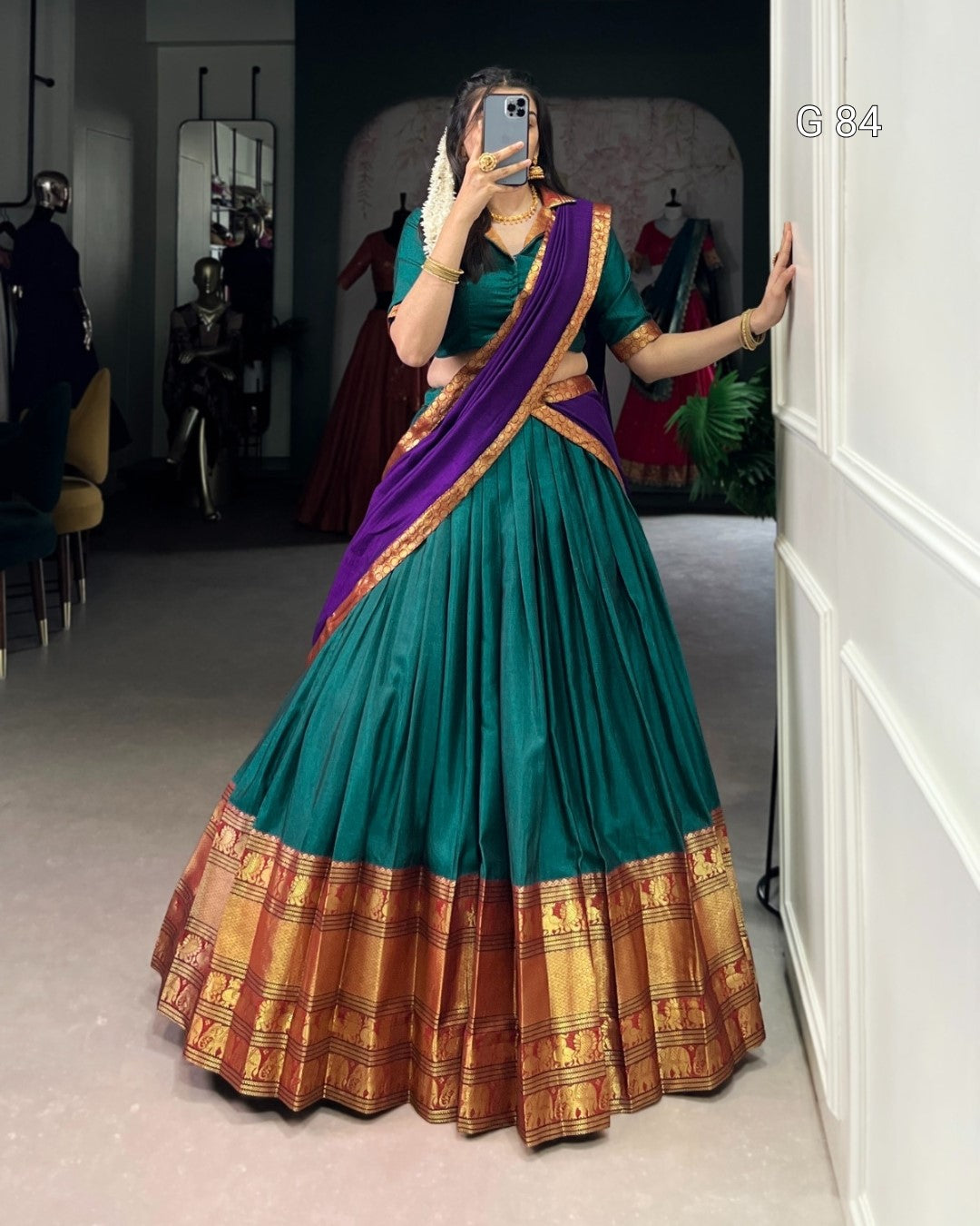 Woman wearing a teal and purple saree with gold border in a room.