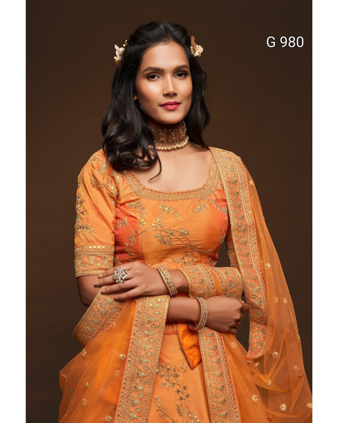 A woman modeling an orange traditional Indian outfit with gold embroidery and a matching sheer dupatta, posed against a dark brown studio background. The text 'G 980' appears in the top right corner.