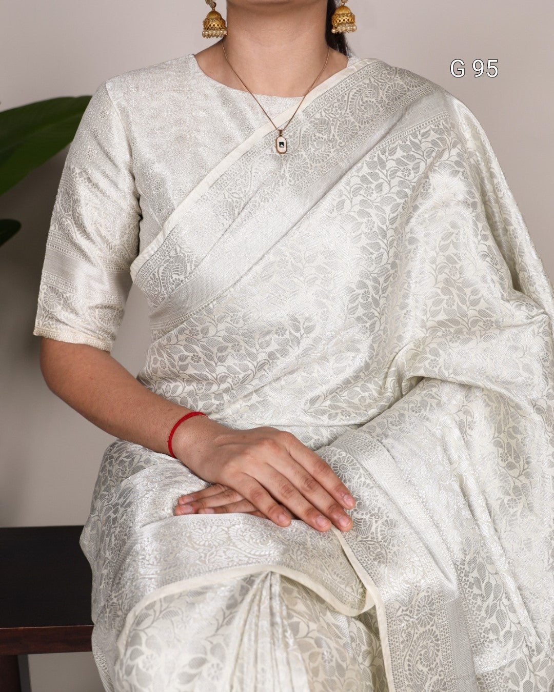 Person wearing a white saree with intricate patterns, sitting indoors.