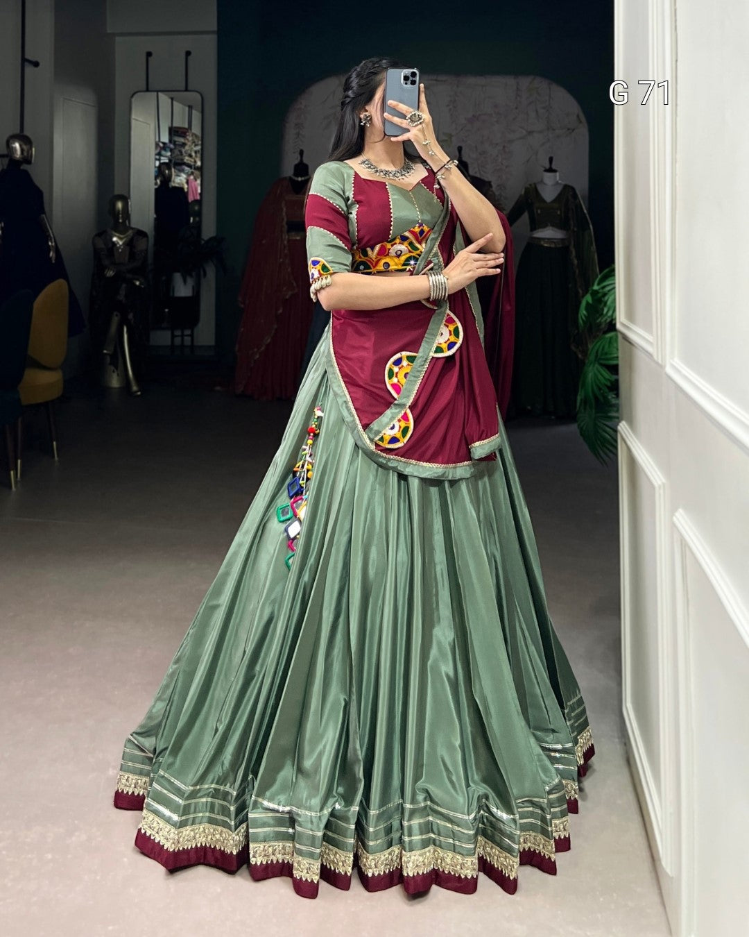 Woman wearing a traditional green and red saree with intricate patterns, standing in a room.