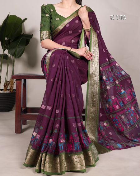 Woman wearing a purple saree with green border, sitting on a chair.