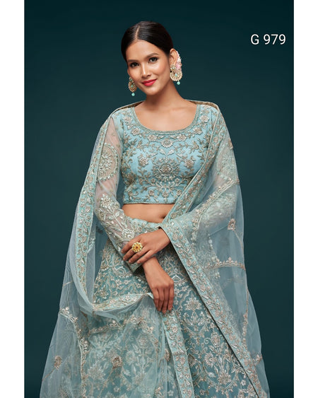 A woman models a light blue embroidered traditional outfit with a matching sheer dupatta, set against a dark teal background. The outfit features intricate gold embroidery and has the text 'G 979' printed in the top right corner.