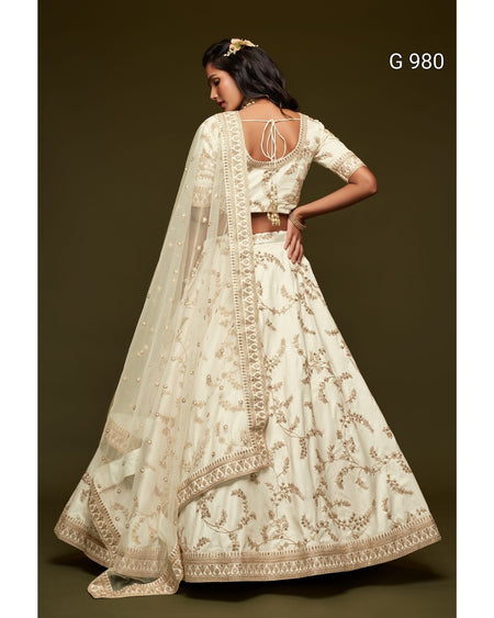 A woman modeling a cream-colored traditional Indian lehenga choli with gold floral embroidery, shown from the back against a dark brown studio background. The text 'G 980' is visible in the top right corner.