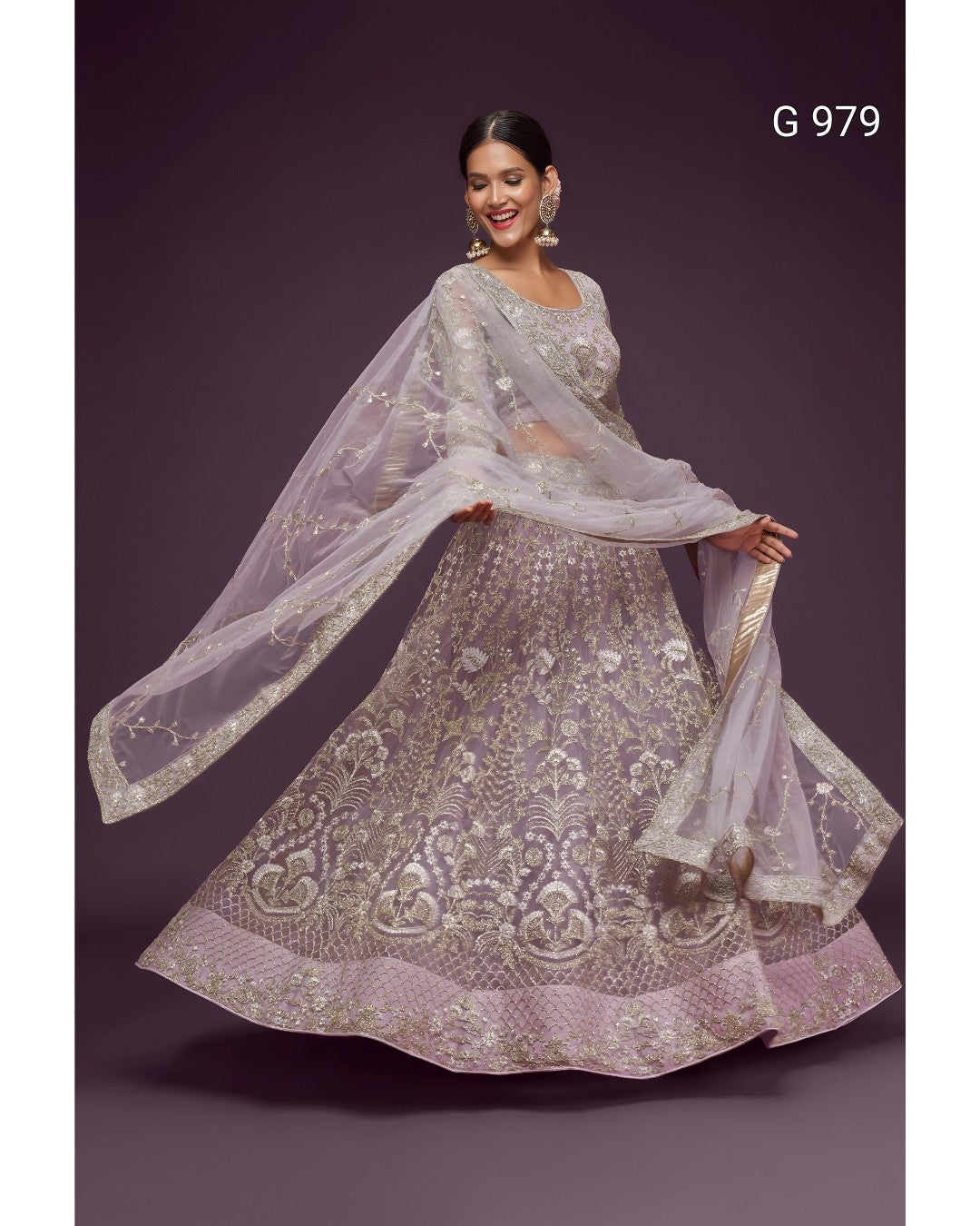 A woman modeling a heavily embroidered light lavender lehenga choli set with a matching sheer dupatta, posed against a dark purple studio background. The text 'G 979' is visible in the top right corner.