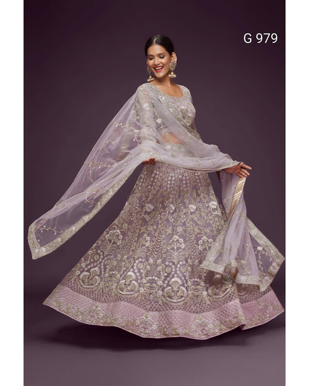 A woman modeling a heavily embroidered light lavender lehenga choli set with a matching sheer dupatta, posed against a dark purple studio background. The text 'G 979' is visible in the top right corner.
