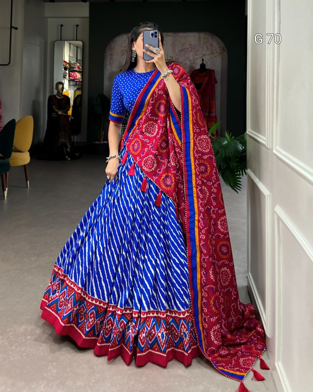 Woman wearing a blue and red saree with a patterned border in a room.