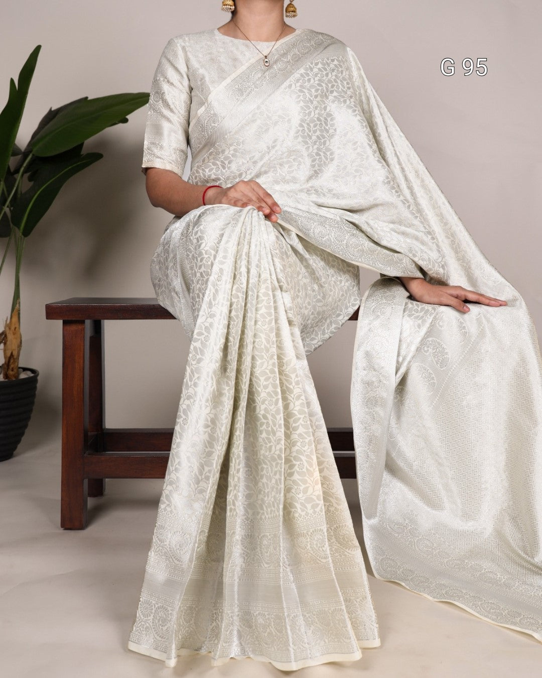Woman wearing a white saree with a subtle pattern, standing against a plain background.