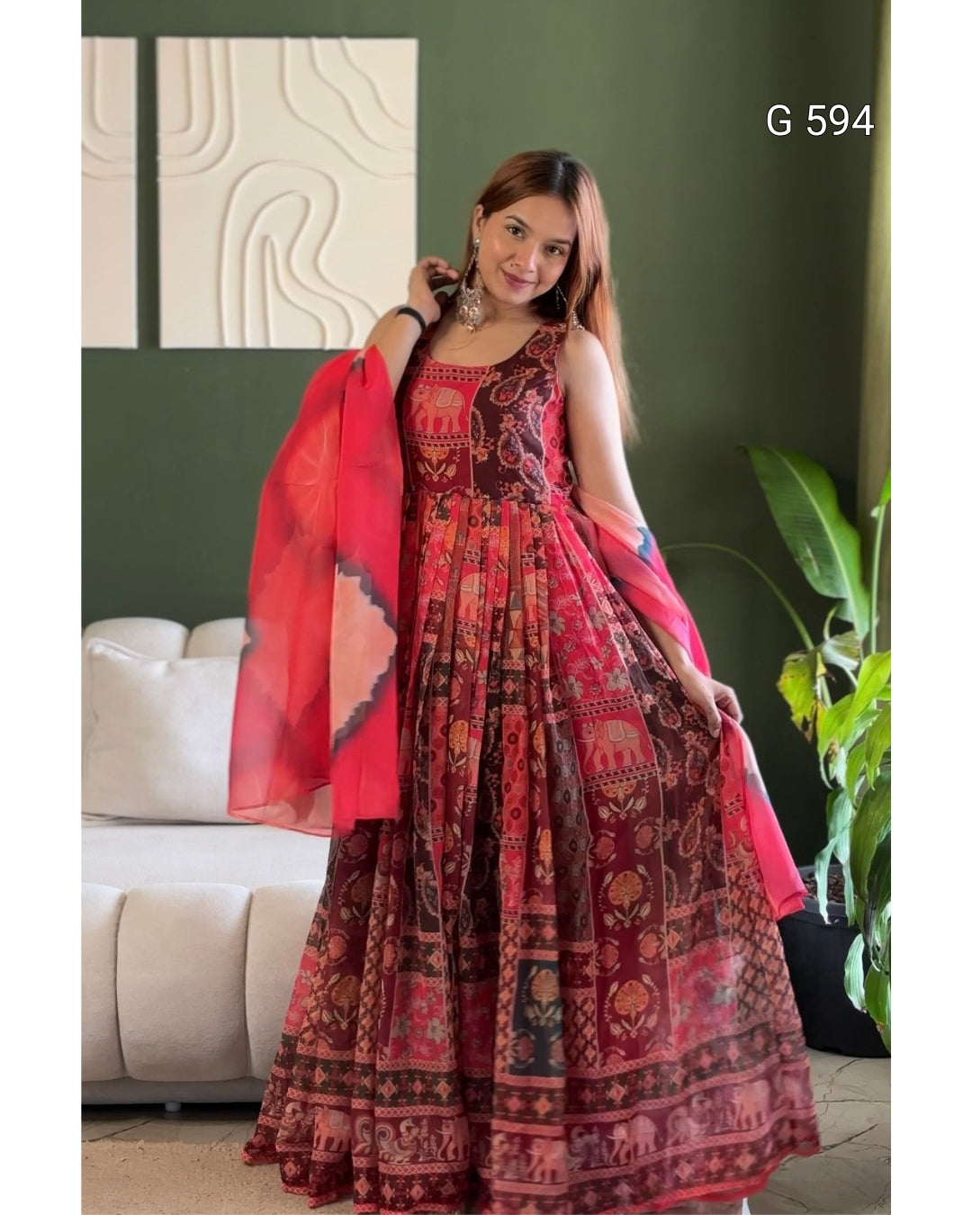 A woman models a red and maroon printed Anarkali gown with a matching dupatta in a living room setting. The dress features intricate traditional patterns and the text 'G 594' is visible in the top right corner.