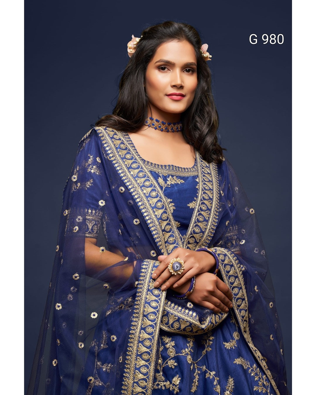 A woman modeling a royal blue traditional outfit with intricate gold embroidery and a matching sheer dupatta, set against a dark navy studio background. The text 'G 980' is visible in the top right corner.