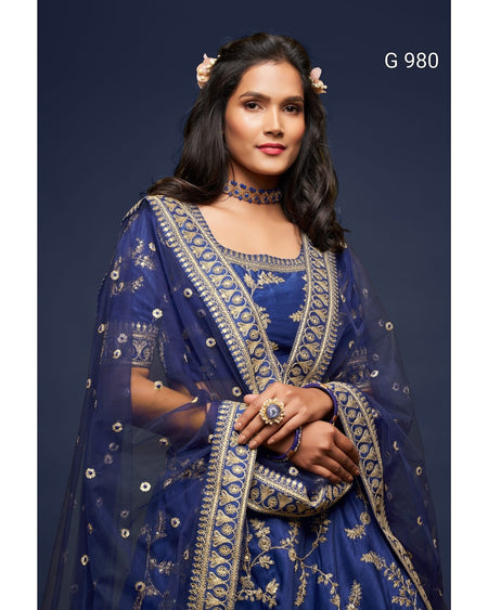 A woman modeling a royal blue traditional outfit with intricate gold embroidery and a matching sheer dupatta, set against a dark navy studio background. The text 'G 980' is visible in the top right corner.