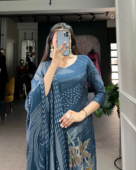 Woman taking a mirror selfie wearing a blue dress with floral patterns in a room.