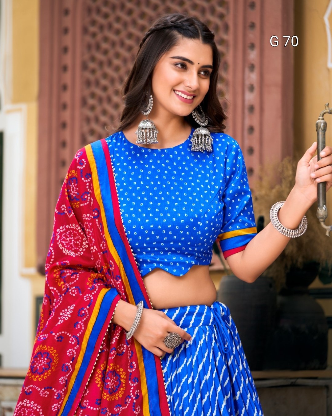 Woman wearing a blue saree with colorful border and jewelry, holding a decorative item.