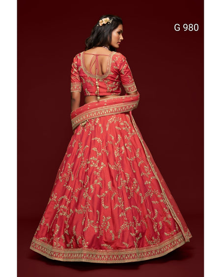 A woman modeling a red and gold embroidered Indian lehenga choli suit from the back, set against a solid dark red background. The text 'G 980' is visible in the top right corner.