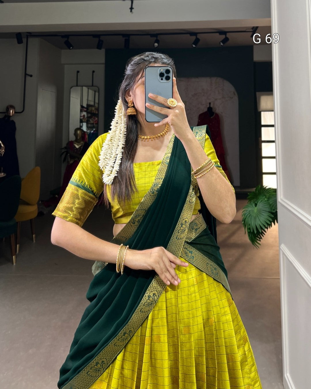 Person wearing a yellow and green saree taking a mirror selfie.
