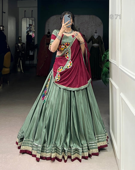 Person wearing a traditional outfit with a green and maroon saree in a room.