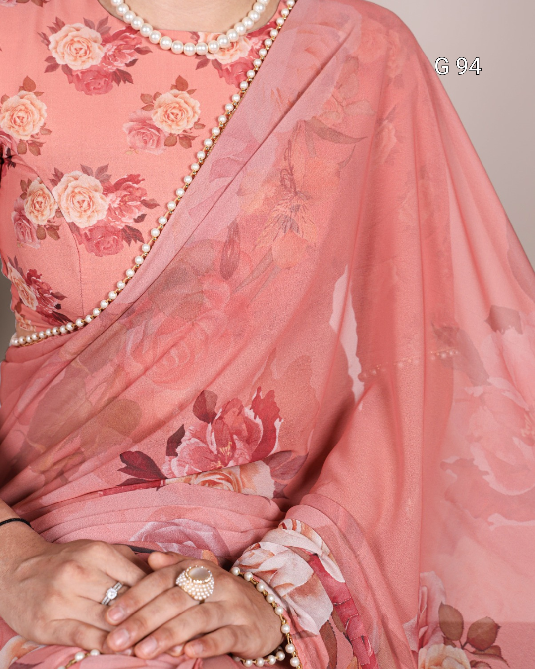 Pink floral saree with a pearl border and jewelry.
